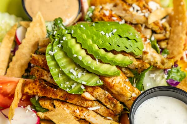 Grilled chicken salad topped with sliced avocado, fresh vegetables, and creamy dressing