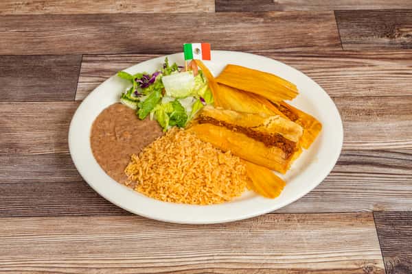 Mexican tamales served with rice, refried beans, lettuce, and tomato