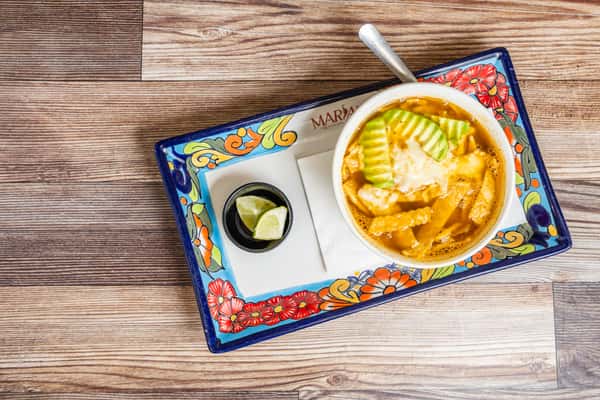 Mexican tortilla soup topped with sliced avocado and served on a colorful platter