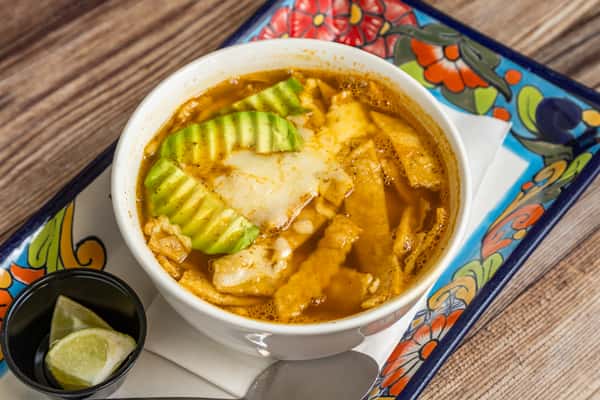Mexican tortilla soup topped with sliced avocado and served with fresh lime