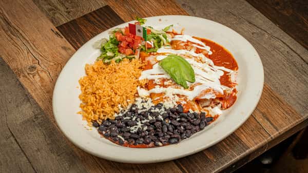 Red enchiladas topped with crema and avocado, served with Mexican rice and black beans