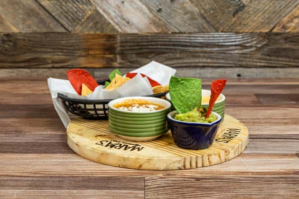Colorful tortilla chips served with a trio of Mexican dips on a wooden board