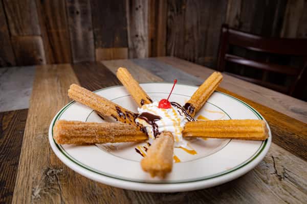Churros with a scoop of ice cream topped with chocolate drizzle, whipped cream and a cherry