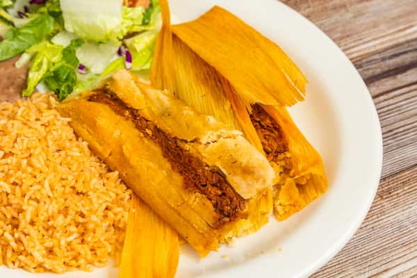 Golden tamales served with Mexican rice and beans on a white plate
