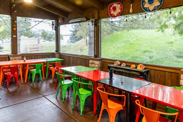 Covered dining patio with colorful chairs, red tables, and views of the surrounding greenery