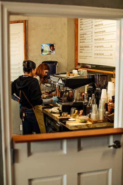 Two baristas working behind a coffee counter, preparing drinks with an espresso machine in a cozy café.