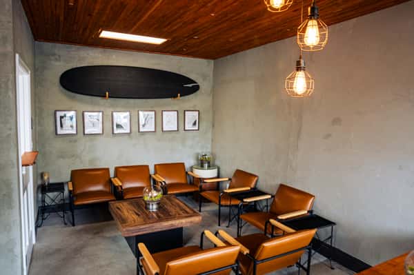 Cozy lounge with leather chairs, wooden table, surfboard wall décor, and hanging pendant lights creating a warm atmosphere.
