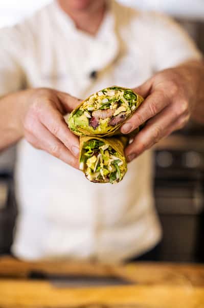 Chef holding a halved wrap filled with greens, eggs, and meat, showcasing the colorful and fresh ingredients inside.