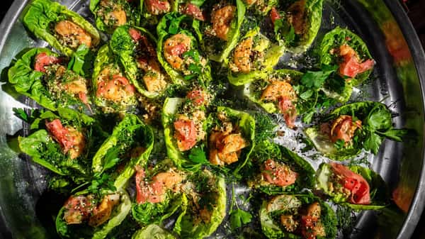 Lettuce cups filled with shrimp, pickled vegetables, sesame seeds, and fresh herbs on a large silver serving tray.