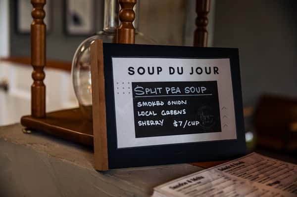 Chalkboard sign reading "Soup du Jour: Split Pea Soup with smoked onion, local greens, sherry - $7/cup."