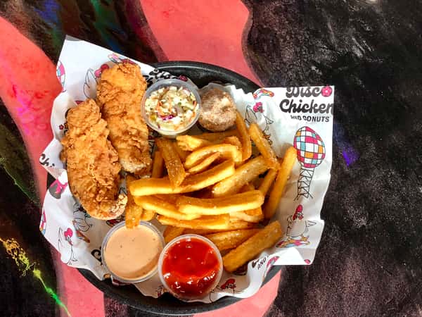 Colorful basket of crispy fried chicken tenders, thick-cut French fries, creamy coleslaw, a cinnamon sugar donut hole, and sides of ketchup and dipping sauce, all served on playful branded paper from a disco-themed chicken and donuts restaurant.