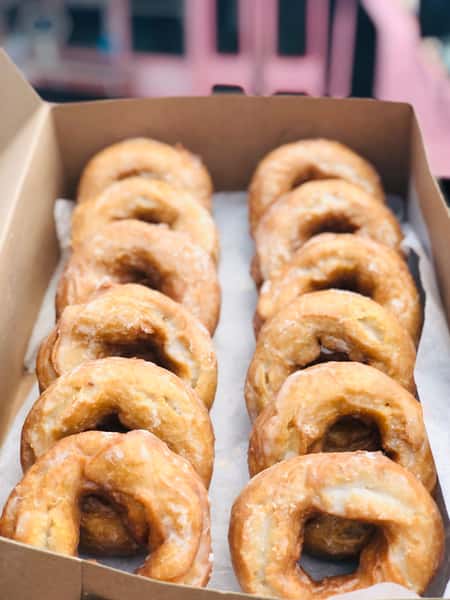 Box of freshly glazed old-fashioned donuts arranged in neat rows, showcasing their golden-brown texture and sweet glaze — a classic treat from a specialty donut shop or food truck.