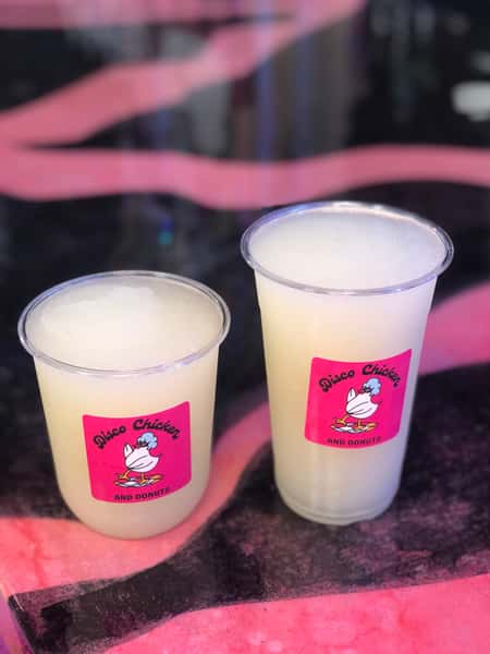 Two frozen lemonades in branded Disco Chicken and Donuts cups, served icy and refreshing on a vibrant pink and black counter — a perfect citrusy treat to complement fried comfort food.