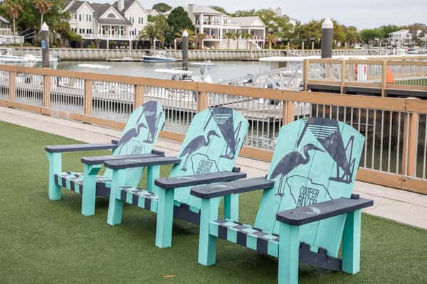 colorful Adirondack chairs on a waterfront lawn overlooking a marina with coastal homes