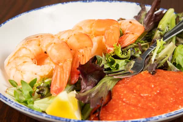 close-up of shrimp cocktail with cocktail sauce and fresh greens on a white plate