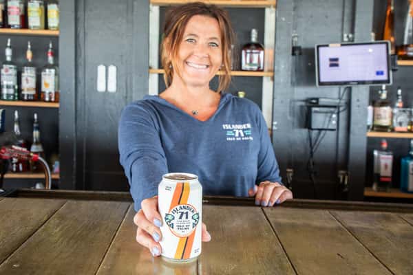 bartender smiling behind the bar holding a canned drink in a casual coastal restaurant