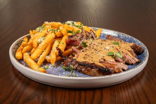 steak frites with sliced grilled steak, crispy fries, and creamy sauce on a rustic plate