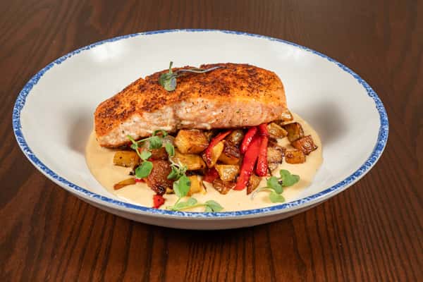 seared salmon fillet served over vegetables with a light sauce on a plated entrée