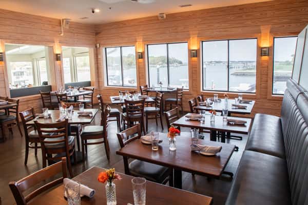 bright waterfront restaurant dining room with wooden tables, booth seating, and large windows overlooking the marina