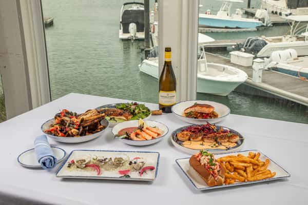 waterfront restaurant table spread with seafood dishes and wine overlooking marina views