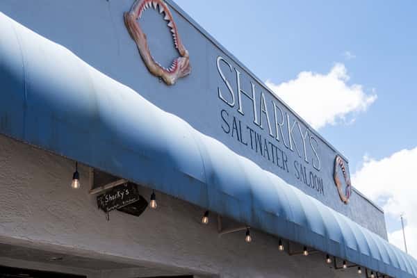 Sharky's restaurant sign on a blue awning with a rope and shell emblem, mounted on the building exterior under a clear blue sky