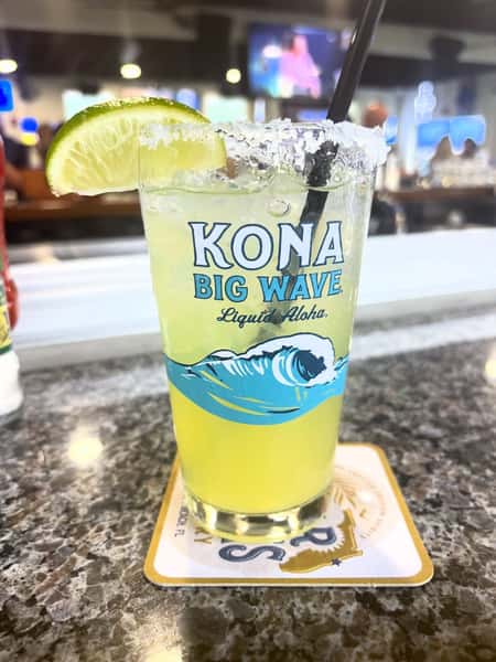 Frozen lime margarita with a salted rim and fresh lime wedge served at a restaurant bar