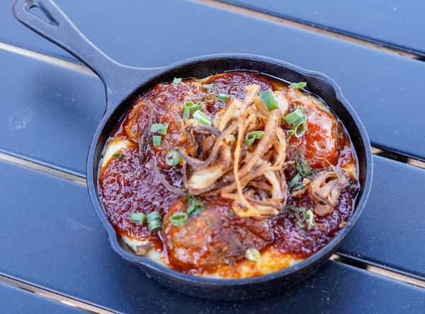 Cast iron skillet meatballs topped with rich marinara sauce, crispy fried onions, and green onions over creamy polenta