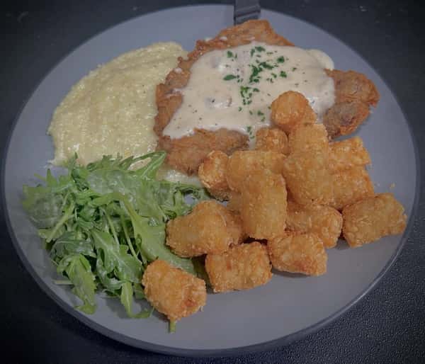 Southern fried chicken plate with creamy grits, crispy tater tots, white gravy, and fresh arugula salad