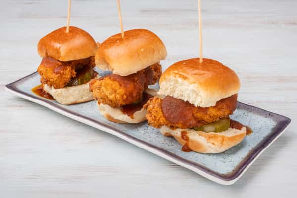 Nashville hot chicken sliders on mini buns, skewered with picks and arranged on a metal serving tray at a restaurant