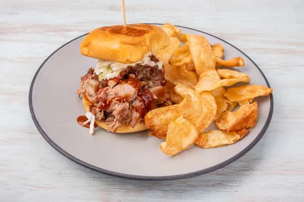 BBQ pulled pork sandwich topped with coleslaw on a bun, served with potato chips on a gray plate at a restaurant