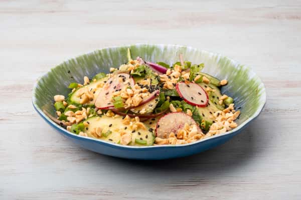 Asian cucumber salad topped with sliced radish, crushed peanuts, and sesame seeds in a blue speckled bowl at a restaurant
