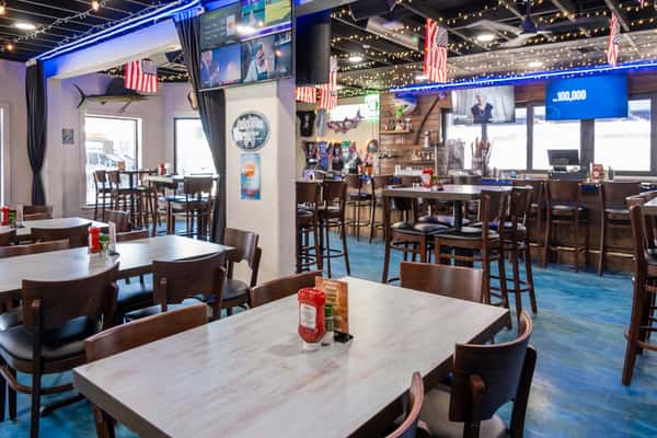 Restaurant dining area with wooden tables, chairs, and condiment caddies, with TVs and nautical decor on the walls