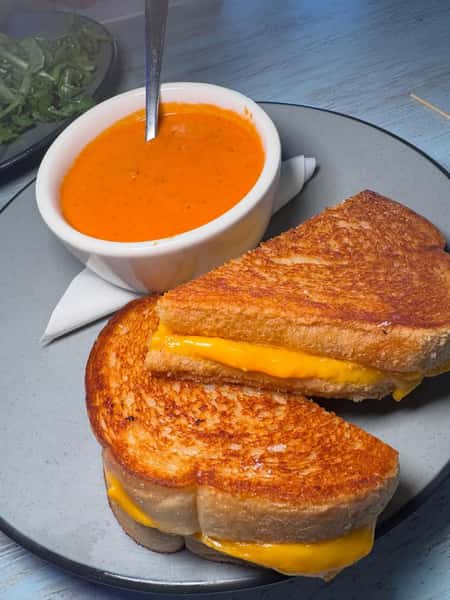 Classic grilled cheese sandwich with melted cheddar cheese served alongside creamy tomato soup
