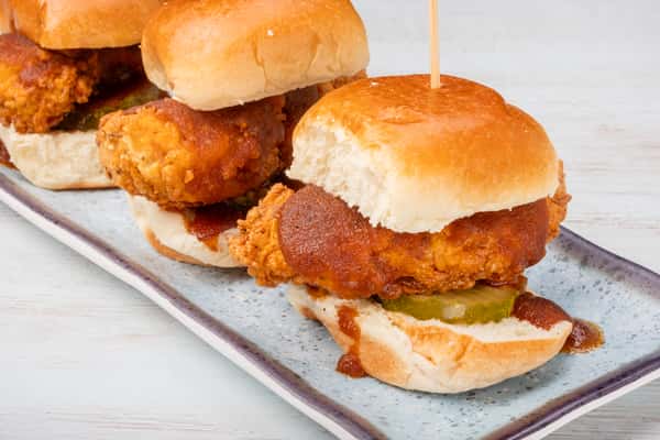 Nashville hot chicken sliders on mini buns, skewered with picks and arranged on a rectangular slate plate at a restaurant