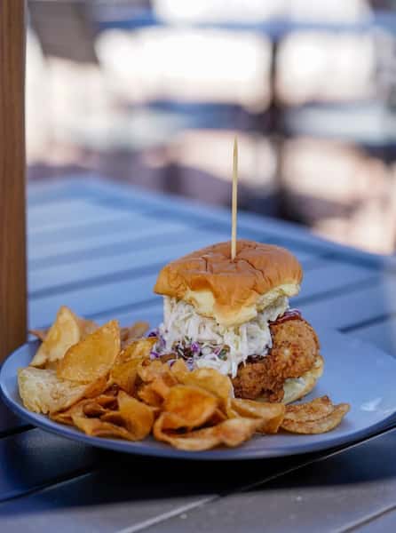 Fried fish sandwich slider with creamy coleslaw and crispy kettle chips served on a toasted bun at an outdoor seafood restaurant