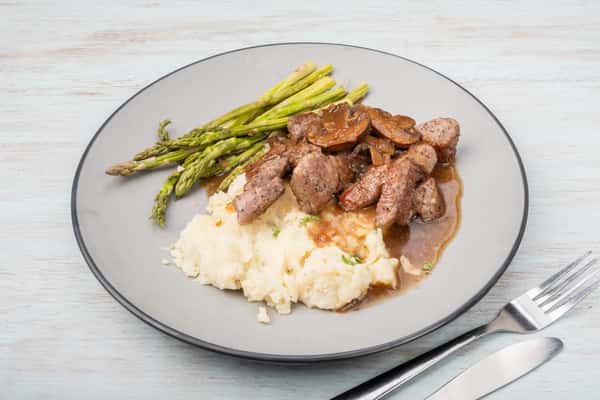 Steak tips with mushroom gravy served over mashed potatoes with asparagus on a gray plate at a restaurant