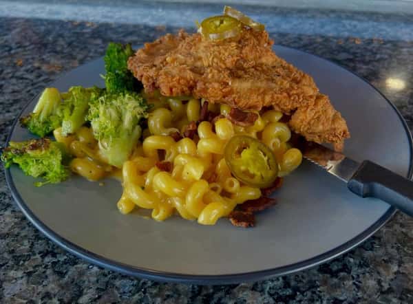 Crispy fried chicken served over jalapeño bacon mac and cheese with roasted broccoli on a restaurant plate