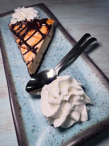 Slice of cookies and cream cheesecake drizzled with chocolate sauce and caramel served with whipped cream