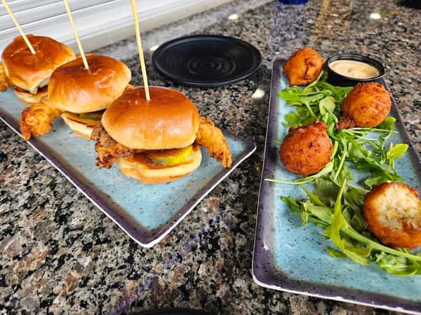 Crispy fried shrimp sliders with pickles on toasted brioche buns served alongside golden hush puppies and creamy dipping sauce