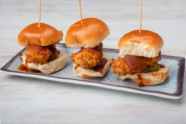 Nashville hot chicken sliders on mini buns, skewered with picks and arranged on a metal serving tray at a restaurant