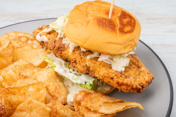 Crispy fried fish sandwich on a toasted bun with house-made slaw and pickles, served with kettle chips at Sharky's NSB, a coastal scratch kitchen and beach bar on Flagler Avenue in New Smyrna Beach.