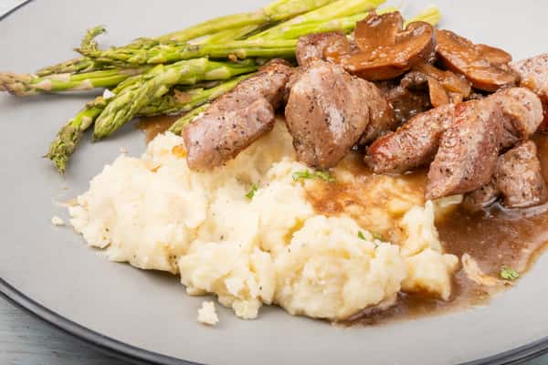 Steak tips smothered in mushroom gravy, served with mashed potatoes and asparagus on a gray plate at a restaurant