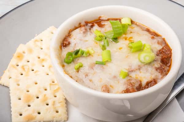 White chicken chili topped with chopped green onions in a white bowl, served with crackers on the side at a restaurant