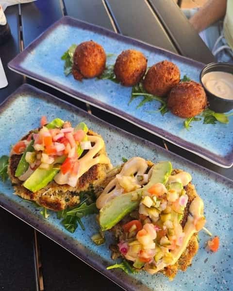 Crab cake appetizers topped with avocado, pico de gallo, and creamy sauce served with fried hush puppies