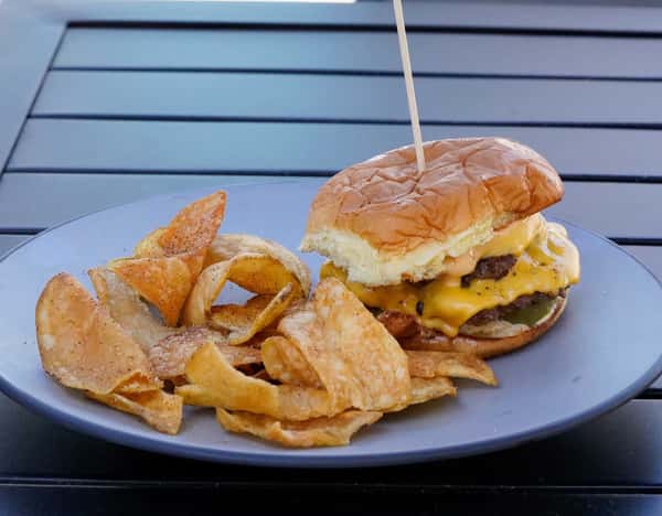 Double cheeseburger slider with melted cheddar, pickles, and house sauce served with crispy kettle chips on a casual dining patio table