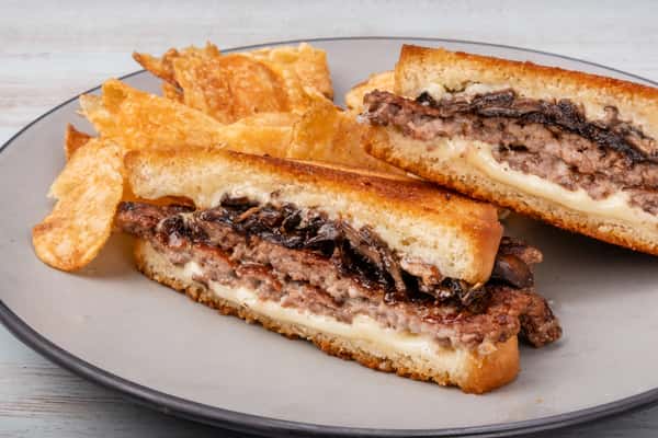 Truffle mushroom patty melt sandwich with melted cheese on grilled bread, cut in half and stacked on a white plate at a restaurant
