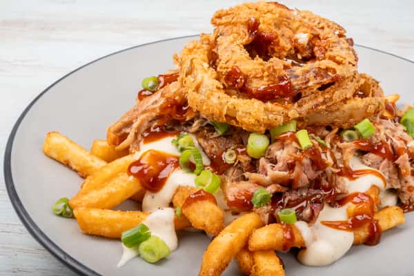 Loaded fries topped with crispy onion straws, cheese sauce, and chopped green onions on a gray plate at a restaurant