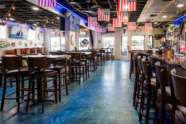 Restaurant dining area with wooden bar stools and tables on a polished blue floor, with American flags hanging from the ceiling