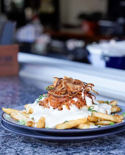Loaded fries topped with creamy white queso, crispy fried onions, and shredded beef at a restaurant bar