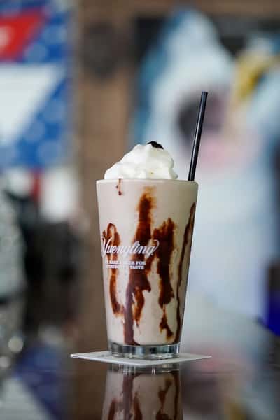 Chocolate milkshake topped with whipped cream and chocolate drizzle served in a frosted bar glass